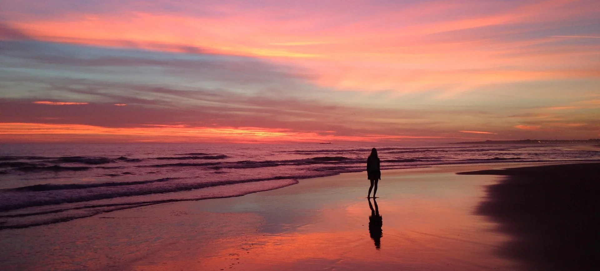 A woman stands at the ocean edge at sunset